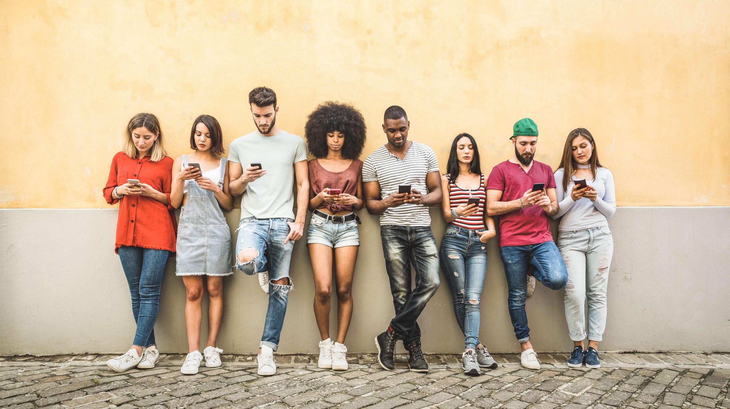 millennials standing against wall looking at phones